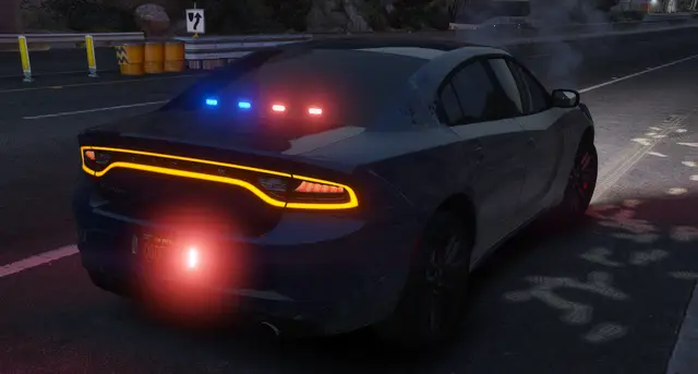 A Charger patrol unit parked on a highway shoulder, amber grille lights on