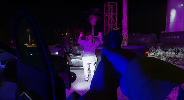 An officer holding a person at gunpoint under purple street lighting