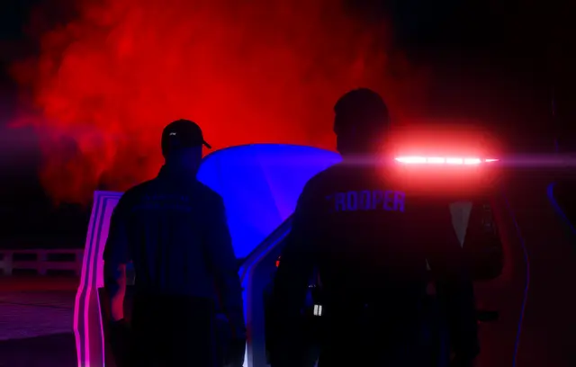 Two figures silhouetted against red and blue emergency lights